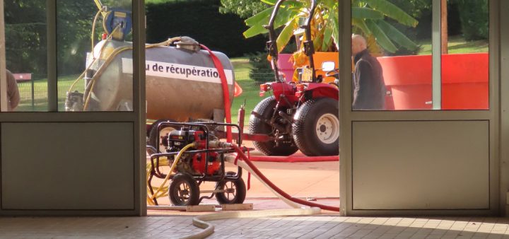 Un petit camion citerne récupérant l'eau d'une piscine pour arroser des plantations.