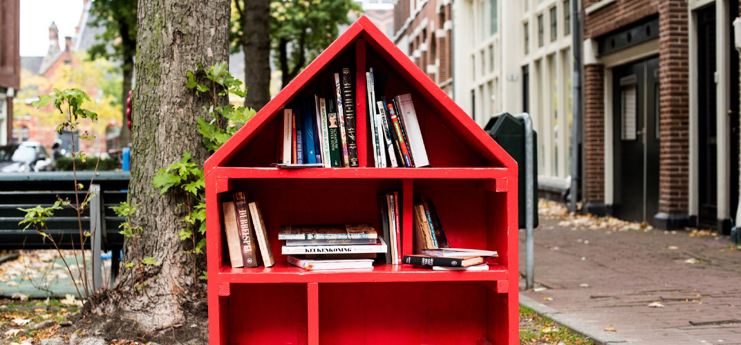 Une boite à livre en bois et en forme de maison dans une rue en ville.